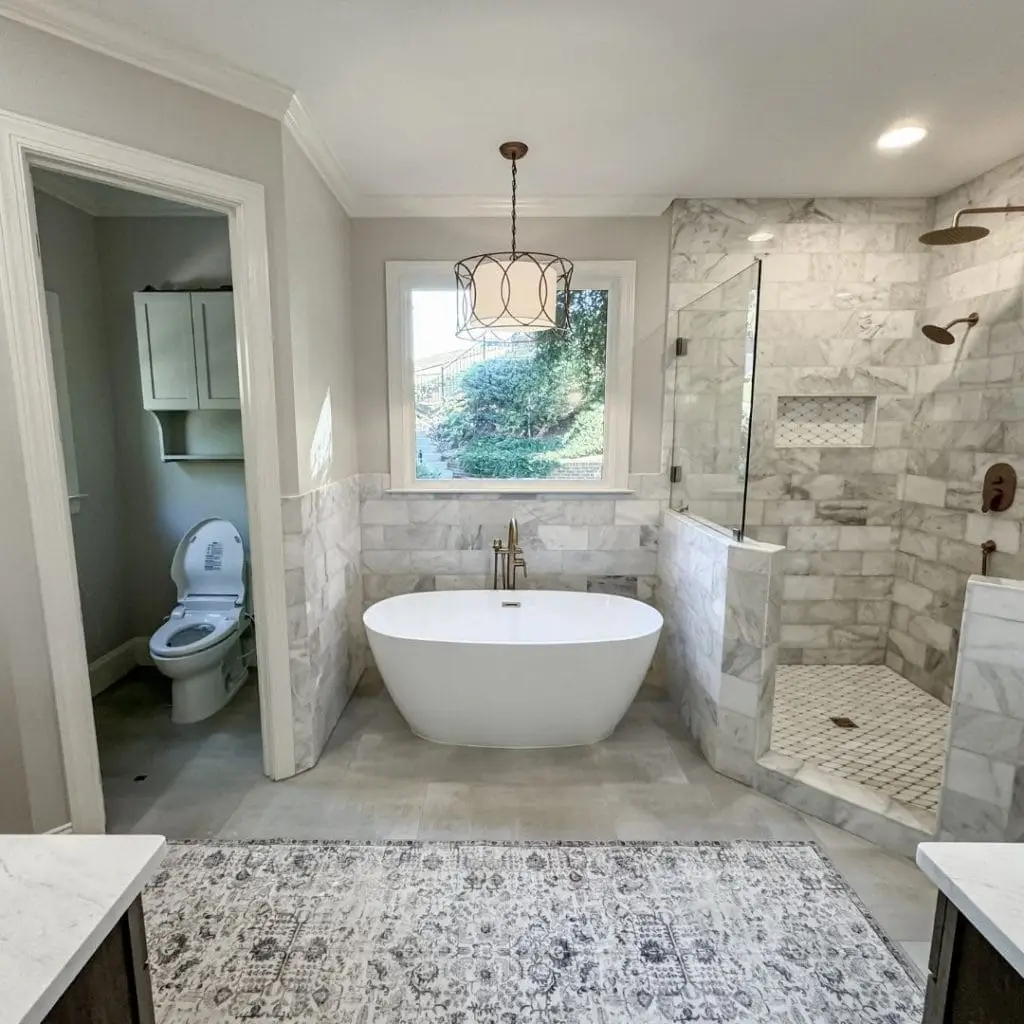A newly remodeled bathroom with smooth tile, a free standing tub, and frameless shower glass.