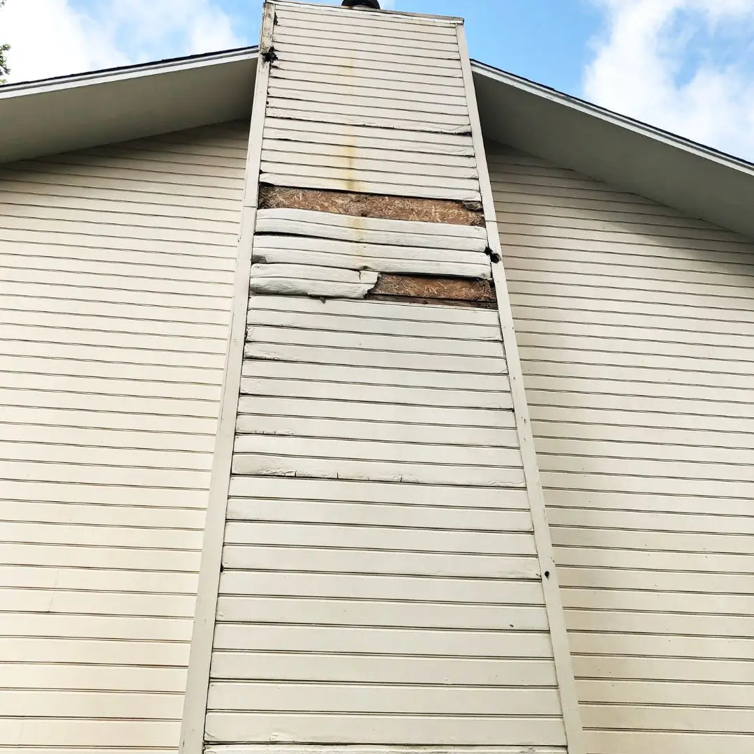A chimney in Pelham, AL, with rotten siding in need of our Masonite siding replacement service.
