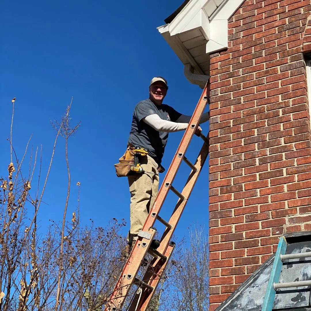 An eaves repair contractor standing on a ladder making repairs to a house in Birmingham.
