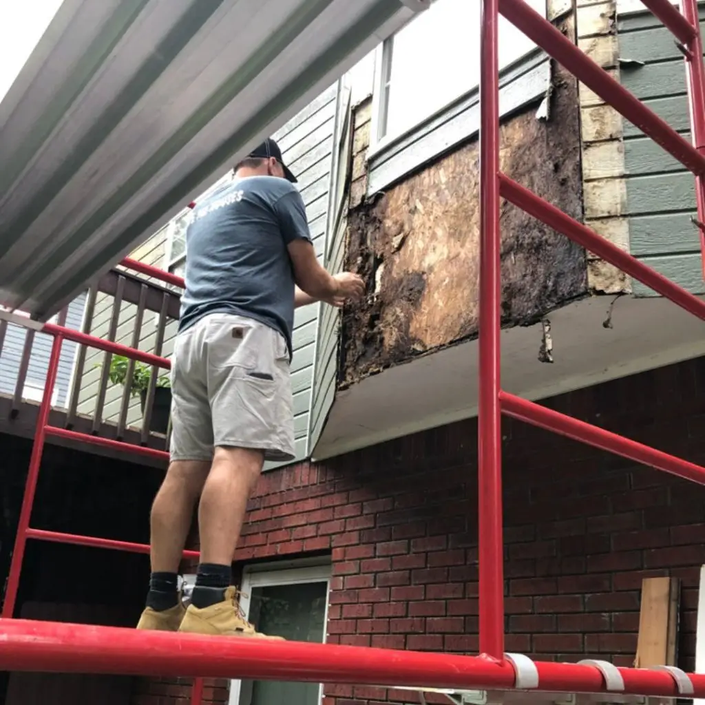 A window repair man removing rotten wood from a bay window.