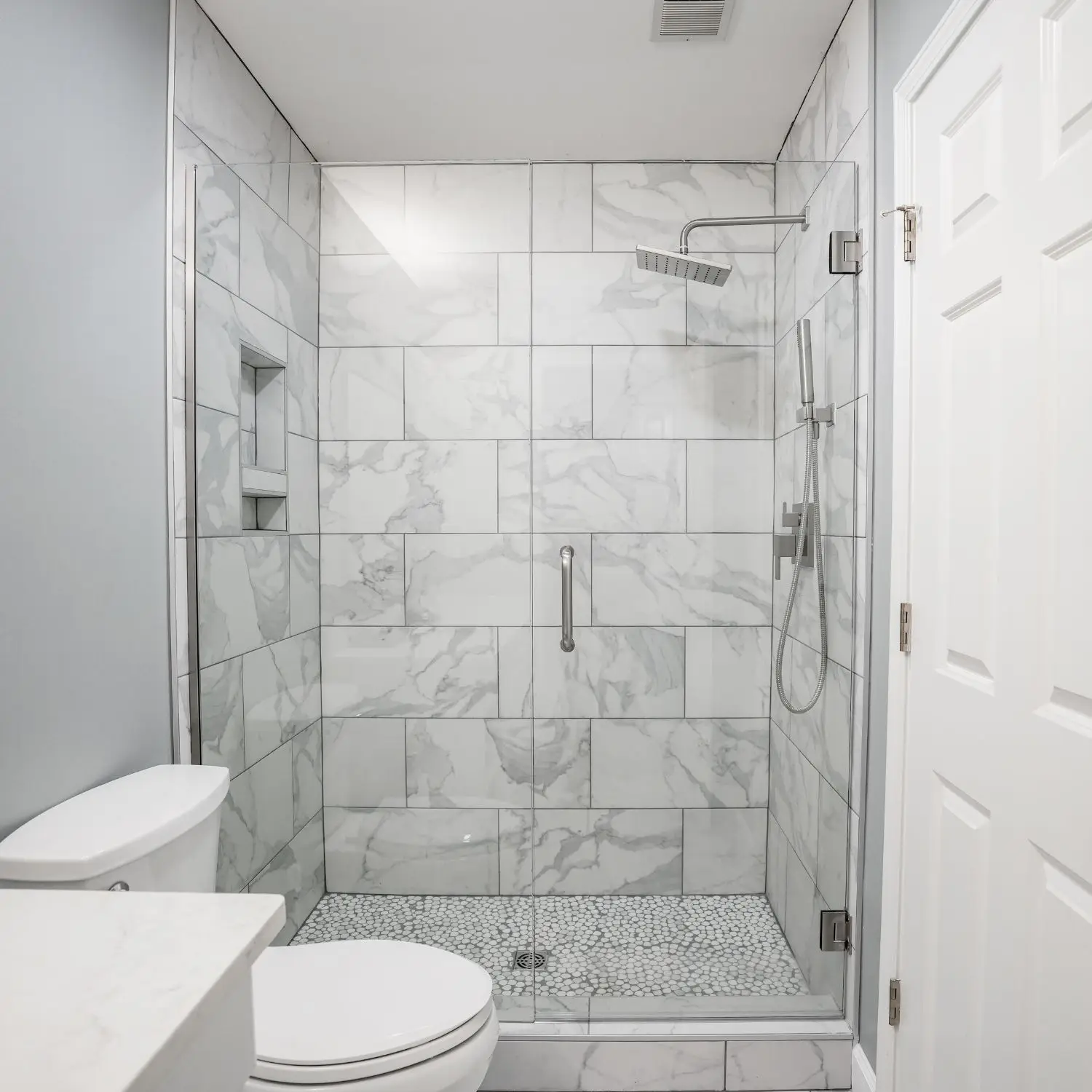A modern shower in Alabaster with marble tile and built-in shelves, showcasing expert bathroom remodeling craftsmanship.