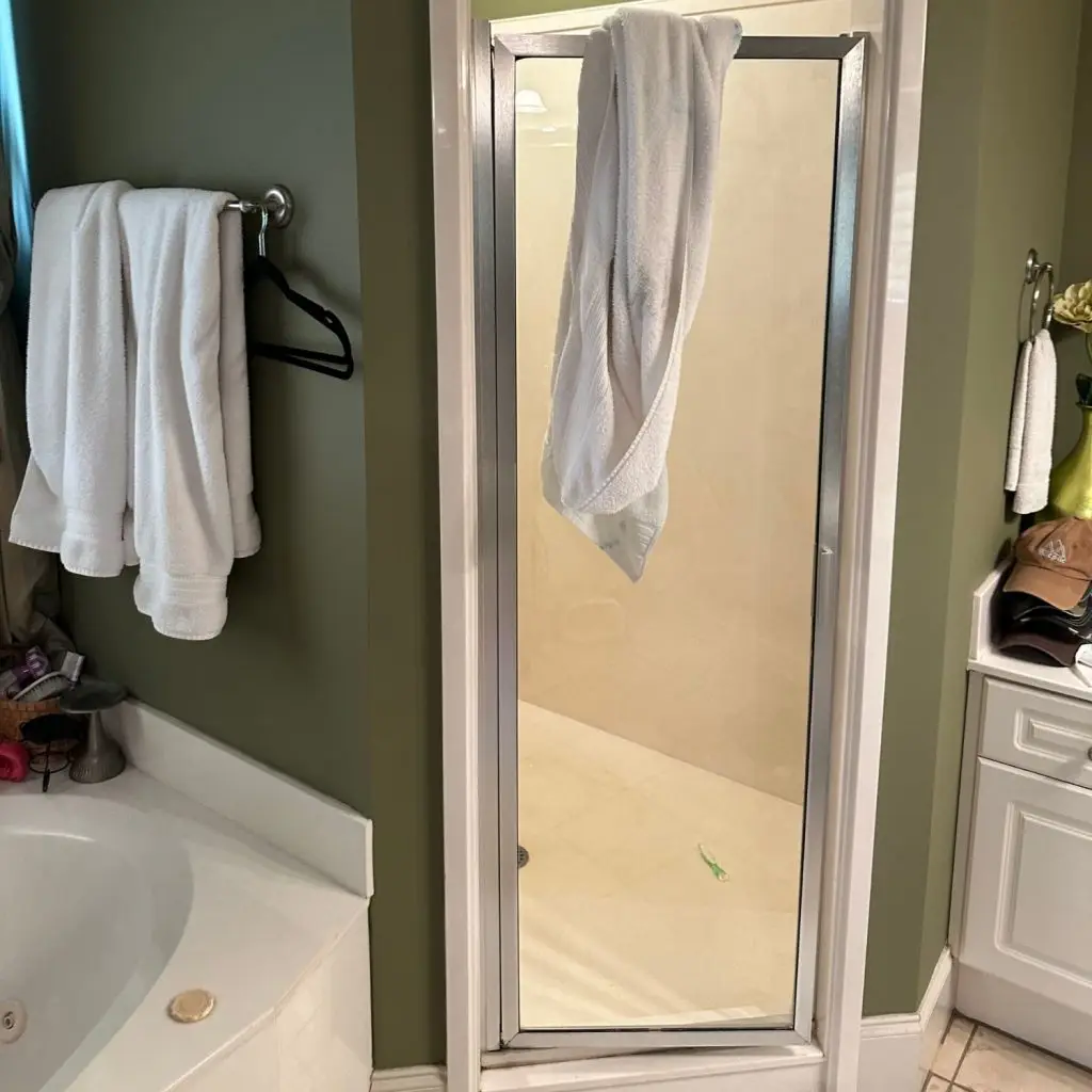 An outdated shower with a basic framed glass door, which can cost $10,000–$15,000 to replace with a walk-in tile shower.