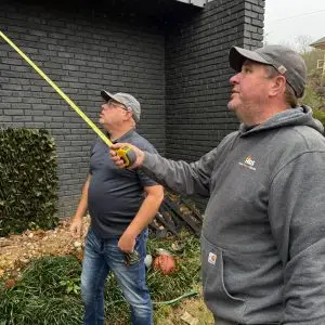 Contractors from Home Repair Service measure and assess the home's exterior before starting the deck replacement project.