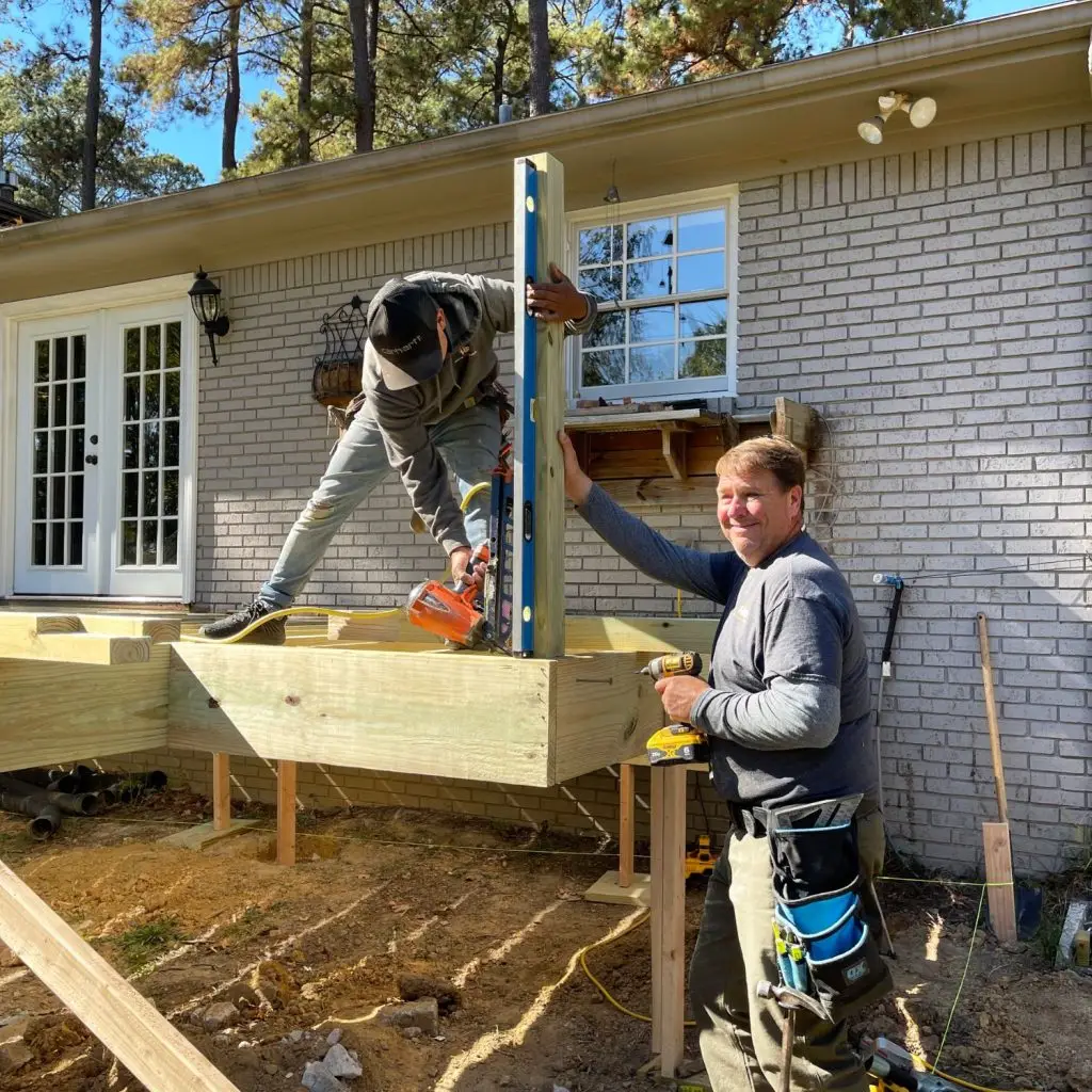 Two professional deck builders working on the frame of a new deck in Birmingham, AL, ensuring posts are level and secure during construction.