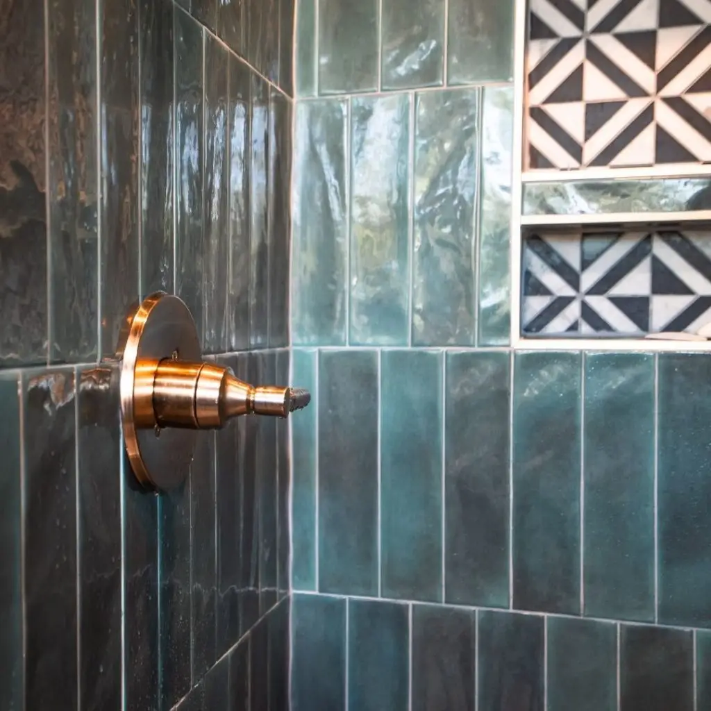 Close-up of a shower wall with glossy green subway tiles and a brushed brass valve.