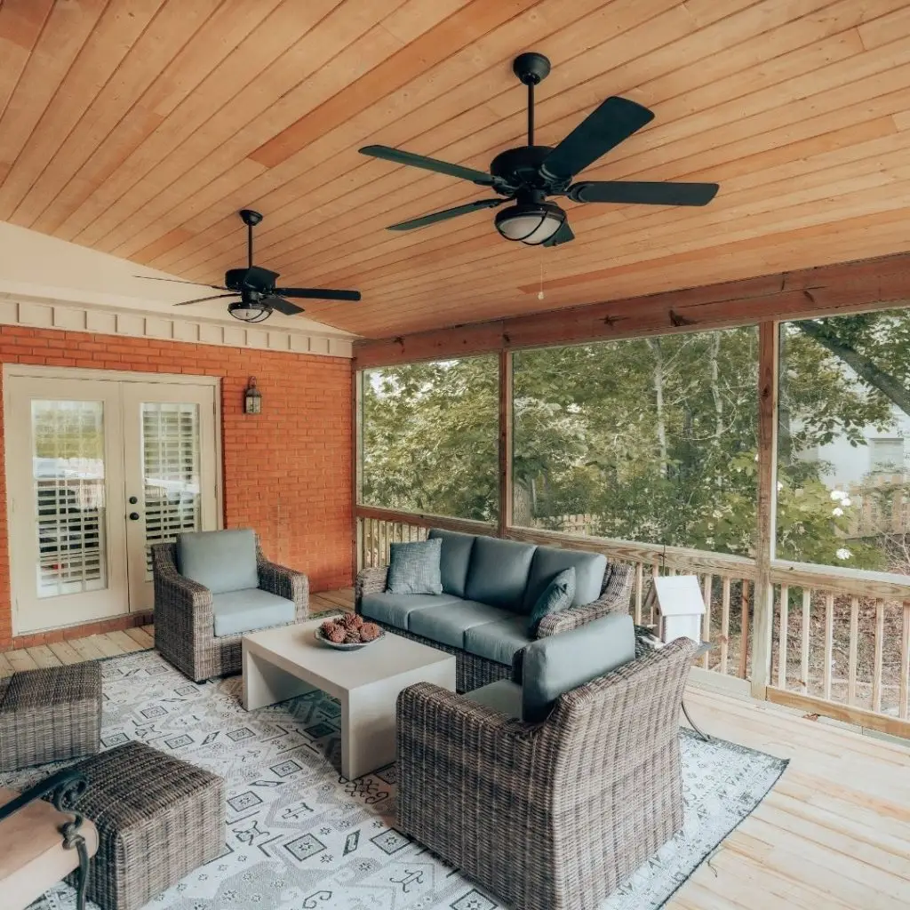 Screened-in porch with stylish seating, ceiling fans, and brick accents, perfect for comfortable outdoor living.