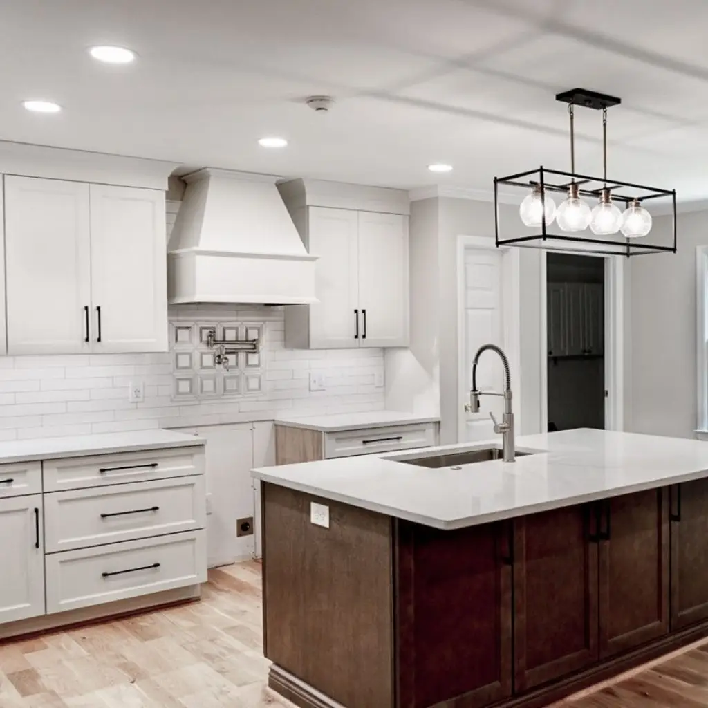 Kitchen remodeling in Mountain Brook featuring a dark wood island, sleek quartz countertops, and white shaker cabinets with black hardware. Custom range hood and modern lighting complete the upscale look.